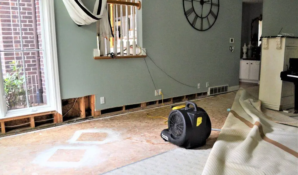 Air movers and a dehumidifier drying a Marietta living room after water extraction, subfloor exposed